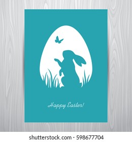 Easter greeting card design with standing rabbit silhouette in an egg shaped white frame. Placed on a grey wooden background.