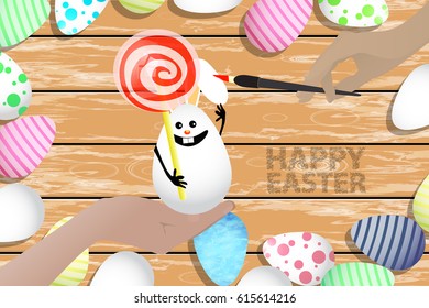 Easter is a perfect illustration for your design. Easter bunny - egg with lollipop in shape ball spiral red-white in hands on a wooden table background in a pile of painted eggs