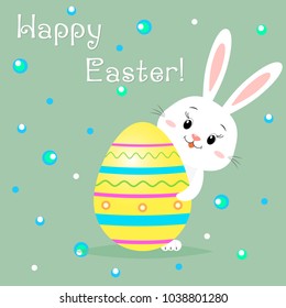 The Easter rabbit peeks out from behind a yellow decorative egg. Congratulations on Easter.