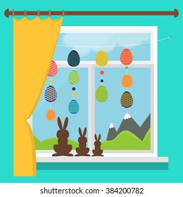 Easter window with garlands of colored Easter eggs. Set of chocolate rabbits on the windowsill.