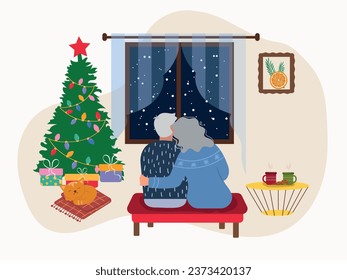 An elderly couple is sitting on a pouf in front of a window in the living room with a Christmas tree. Christmas tree with gifts in the living room with a cat sleeping next to it. Happy New Year and