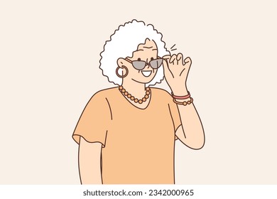 Elderly fashionable woman takes off sunglasses and smiles, feeling zest for life after retirement. Gray-haired grandmother in fashionable clothes and stylish accessories, for concept active old age