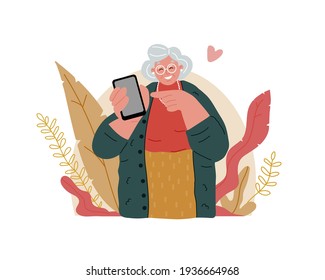 An Elderly Grandmother Is Holding A Cell Phone. She Smiles And Points Her Finger At It. Senior People Using Smart Devices.