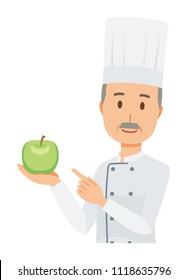 An elderly male chef wearing a cook coat has a green apple