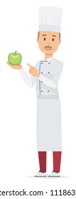 An elderly male chef wearing a cook coat has a green apple