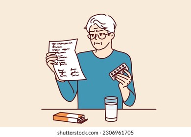 Elderly man takes medicine and reads dosage instructions for pills prescribed by doctor. Gray-haired elderly human is studying instructions to learn about contraindications and side effects of pills.