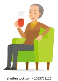 An elderly man wearing brown clothes is sitting on a sofa and drinking coffee