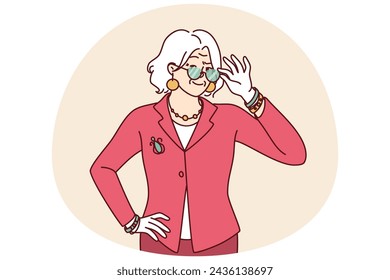 Elderly woman in elegant suit for going to work or dinner party adjusts glasses in front of eyes. Gray-haired grandmother of retirement age dressed in fashionable elegant clothes looks at camera