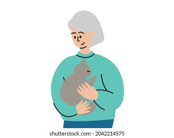 An elderly woman holds a cat in her arms. A woman with gray hair and a gray cat in her arms