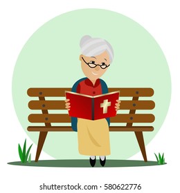 Elderly woman reads the Bible while sitting on a park bench.