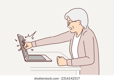 Elderly woman smashes laptop screen by punching it because of bad news on website or freezing software. Gray-haired female pensioner is nervous and breaks laptop while learning to use internet