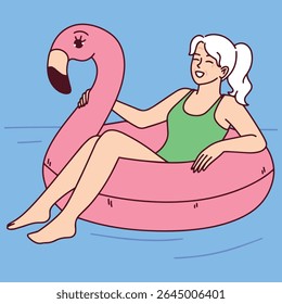 Mulher idosa de maiô relaxa no flamingo inflável flutuando enquanto desfruta de clima quente de verão e calma na piscina