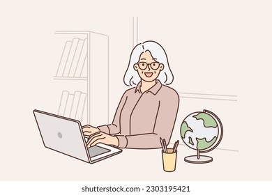 Una profesora de la tercera edad usa una laptop sentada en la mesa con el mundo y enseñando a los estudiantes a través de Internet. El profesor de la tercera edad dirige las clases en línea para los niños de la escuela y da conocimientos de geografía