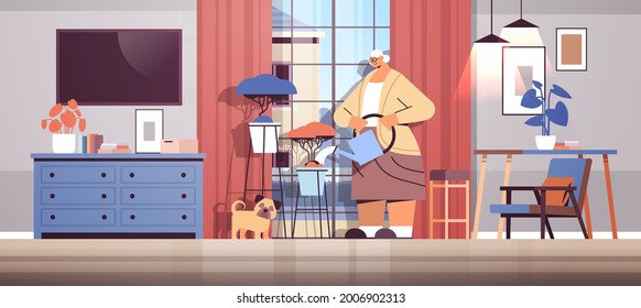 elderly woman watering flowers from watering can senior housewife taking care of house plants living room interior
