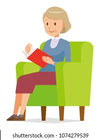 An elderly woman wearing blue clothes is reading on a sofa