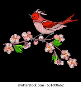 Embroidery bird and sakura blossom flowers on branch of tree isolated on black background.