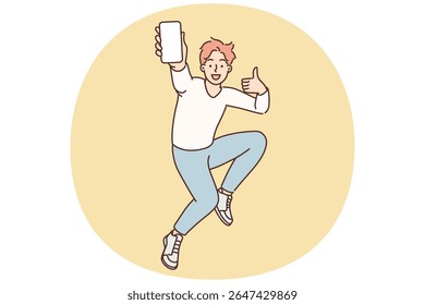 Encouraged man jumps up with mobile phone in hands showing blank screen of gadget and shows thumbs up. Excited teenager guy with smartphone advertises mobile app or website for young people