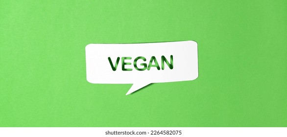 English text vegan in paper speech bubble punched out on green paper background. Photorealistic vector in banner format. 