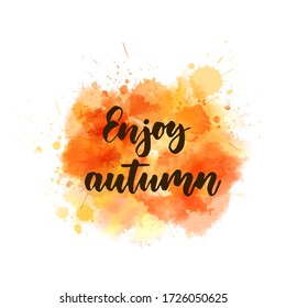 Enjoy autumn - handwritten modern calligraphy lettering on abstract watercolor splash. Season illustration. Orange colored.