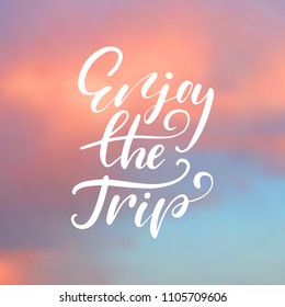 Enjoy the trip - handwritten lettering, summer holiday quote on abstract blur unfocused sky backdrop