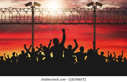 Enraged crowd of people are behind bars. Fence wire mesh barbed wire, vector silhouette. Street camera on the pillar. Sunset background. (Clipping Mask)