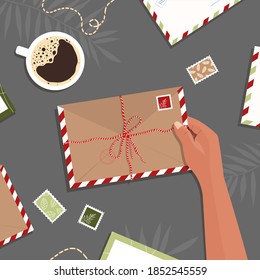 Envelope in hand on table background, hand drawn letters and postcards on workspace in flat style. The woman opens the package. Vector stock illustration