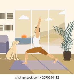 European appearance young man staying in Warrior 1 or Virabhadrasana I posture, doing yoga at home early morning, at sunrise, in the room with the view on mountains and sea, dog sitting nearby. 