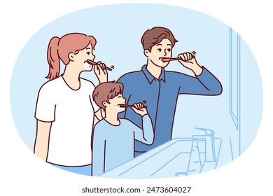 Family brushes teeth together standing in bathroom near mirror to teach boy morning hygiene procedures. Mom and dad with son use toothbrushes to clean mouth after eating to avoid teeth caries