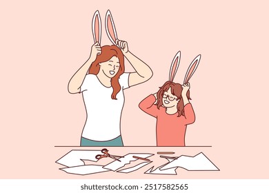 Family creativity for mom and daughter cutting out bunny ears from paper or preparing for christmas masquerade. Older and younger sister are engaged in family creativity, enjoying live communication