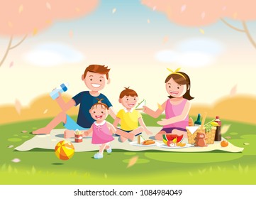 Family enjoying picnic. They are sitting on the grass in a park, the basket with meal and toys for the kids. Blurred background. 