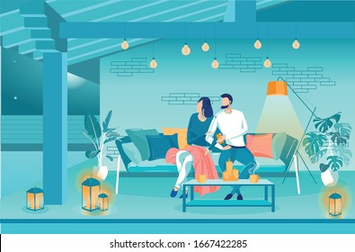 Family Evening on Terrace Listening to Music. Husband and Wife are Sitting on Sofa on Terrace, Cute Luminous Bulbs Hanging from above. Many Candles Create Cozy Atmosphere. On Table Cups Hot Drinks.