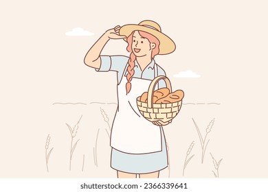 Farmer woman stands in wheat field with spikelets and smiles, holds basket with fresh bread. Cheerful girl is engaged in cultivation of organic wheat and grains for production of delicious buns