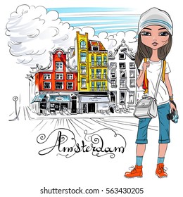 Fashionable hipster girl tourist in a leather jacket, jeans and red boots walking down the street in Amsterdam with traditional Dutch house