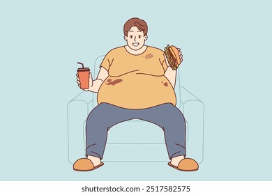 Fat man suffers from obesity caused by problem of overeating and smiles, sitting on sofa with burger and soda in hands. Fat guy eats junk food due to lack of willpower or genetic disease