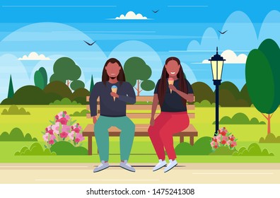 fat obese couple sitting on wooden bench eating ice cream overweight african american man woman having fun unhealthy nutrition obesity concept summer park landscape full length flat horizontal