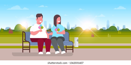 fat obese couple sitting wooden bench eating ice cream overweight man woman having fun relaxing in city park sunset cityscape background full length flat horizontal