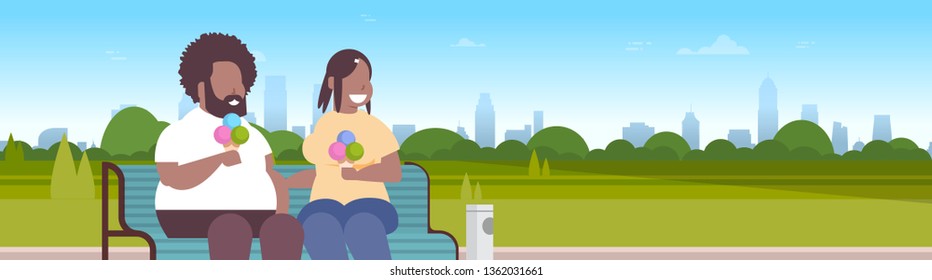 fat obese couple sitting wooden bench eating ice cream overweight african american man woman having fun relaxing in city park sunset cityscape background portrait flat horizontal