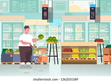 fat obese man with shopping trolley cart choosing vegetables and fruits overweight guy supermarket customer weight loss concept grocery shop interior horizontal full length