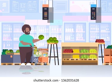 fat obese man with shopping trolley cart choosing vegetables and fruits overweight african american guy supermarket customer weight loss concept grocery shop interior horizontal full length