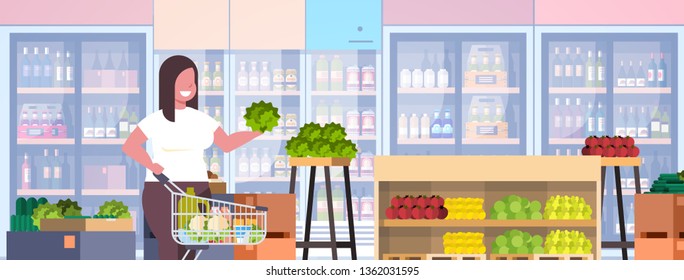 fat obese woman with shopping trolley cart choosing vegetables and fruits weight loss concept overweight girl supermarket customer grocery shop interior horizontal portrait