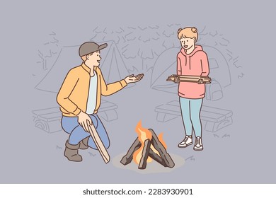 Vater und Tochter machen zusammen Feuer während der Familiencampingreise und machen gemeinsam einen Ausflug in die Natur. Wanderfamilie, die Holz auf Feuer wirft, um warm zu bleiben oder Essen auf dem Parkplatz auf dem Campingplatz zu kochen 