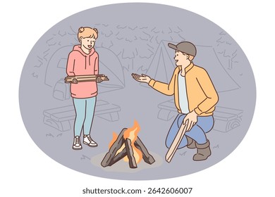 Father and daughter make fire together during family camping trip and enjoy trip to nature together. Hiking family throwing wood on bonfire to keep warm or cook food in parking lot at campsite