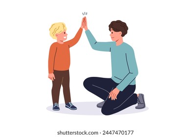 Father supports young son by high-fiving boy and raising child on own after divorce from mother. Young single dad smiles while communicating with son, celebrating father family day