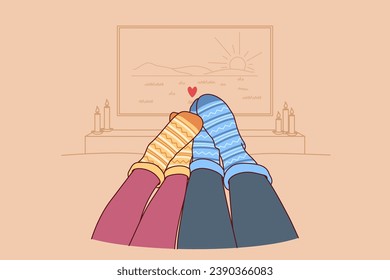 Feet of loving couple in autumn warm socks lying on sofa and watching TV in romantic home atmosphere. Couple spending time together and enjoying comfort during autumn weekend or vacation