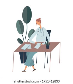 Female doctor sitting at table and making notes in documents while doing paperwork near potted plant in office during work in modern clinic
