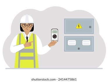 A female electrical engineer holds a digital multimeter in his hand and stands next to an electrical cabinet.