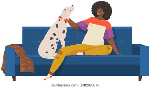 Female pet owner sitting and playing with dog on couch. Caring for animals, joint pastime with pets concept. African lady with domestic animal on sofa. Girl with dalmatian spends time at home