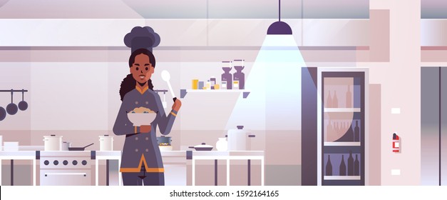 female professional chef cook holding plate with porridge and spoon african american woman in uniform tasting dish cooking food concept modern restaurant kitchen interior flat portrait horizontal