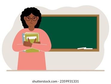 Female teacher with books on the background of the school board.