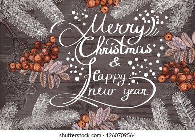 Fir branches with winter Rowan berries on the background of wooden boards. Hand lettering happy New year and merry Christmas.